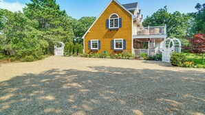 A two-story house with a gravel driveway, a front porch, and a garden. - Summer Beach Pass: Wooded Martha's Vineyard Escape (Vineyard Haven)