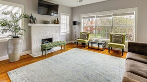 A living room with a fireplace, green armchairs, a bench, and a large vase. - Apt Near Hermann Park & TMC - Free Parking Spot! (Houston)