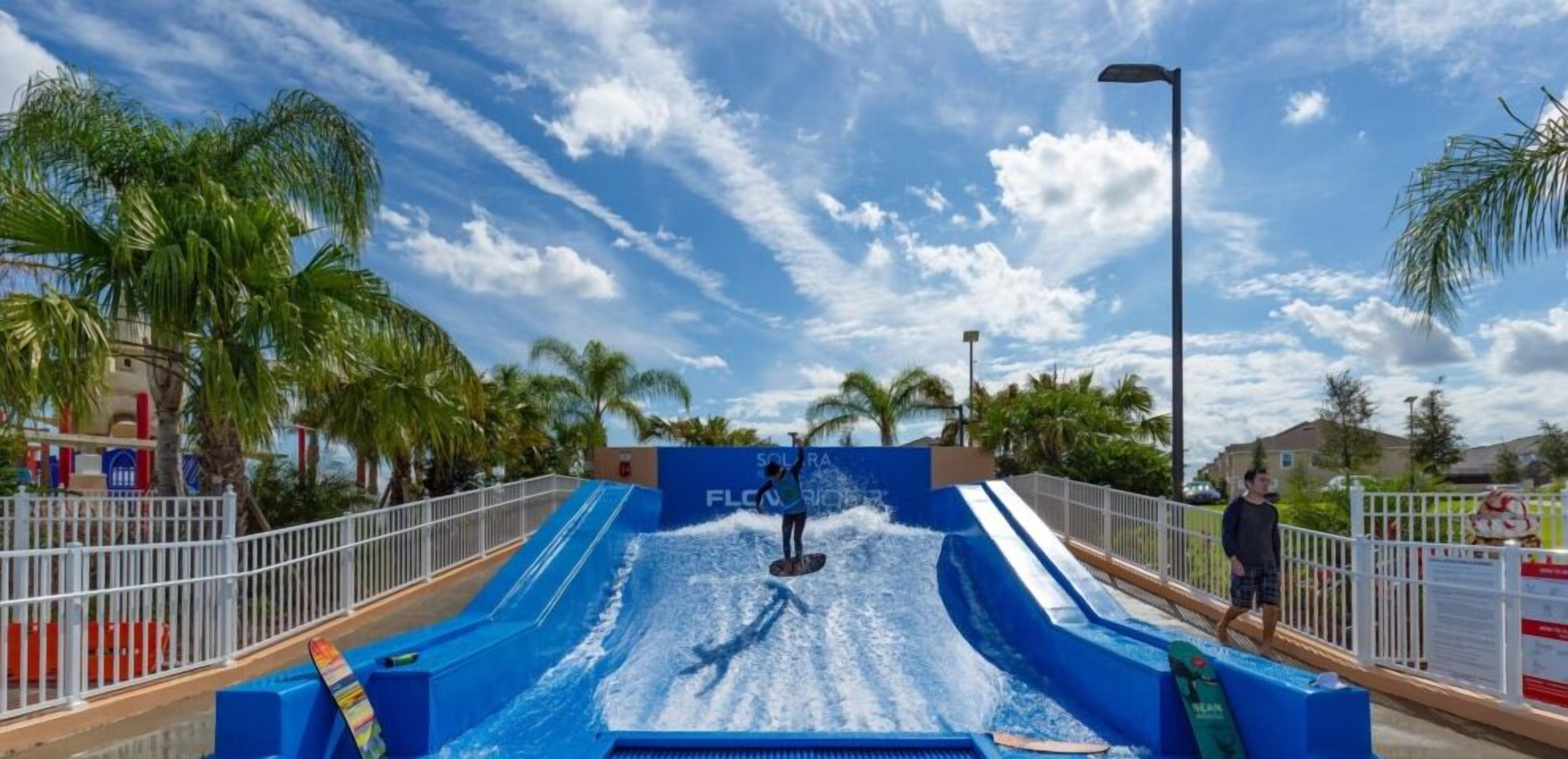 A water slide with a person at the top, surrounded by palm trees and a clear sky.