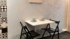 A small dining area with a white table and two black chairs, a patterned wall, and a simple line art painting above the table. - Paris 4U Studio (Paris)