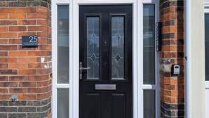 Una puerta principal negra con un panel de vidrio, un buzón y una placa con el número de la casa.