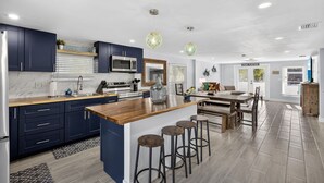 A modern kitchen with dark blue cabinets, a wooden island, and bar stools. - Spacious 5-bedroom/4-bathroom house. Less than 1 block to beach! Free Wine! (Fort Myers Beach)