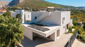 A modern building with a flat roof, solar panels, and a view of a mountain. - Luxury Villa Nikandra with Pool (Žrnovnica)