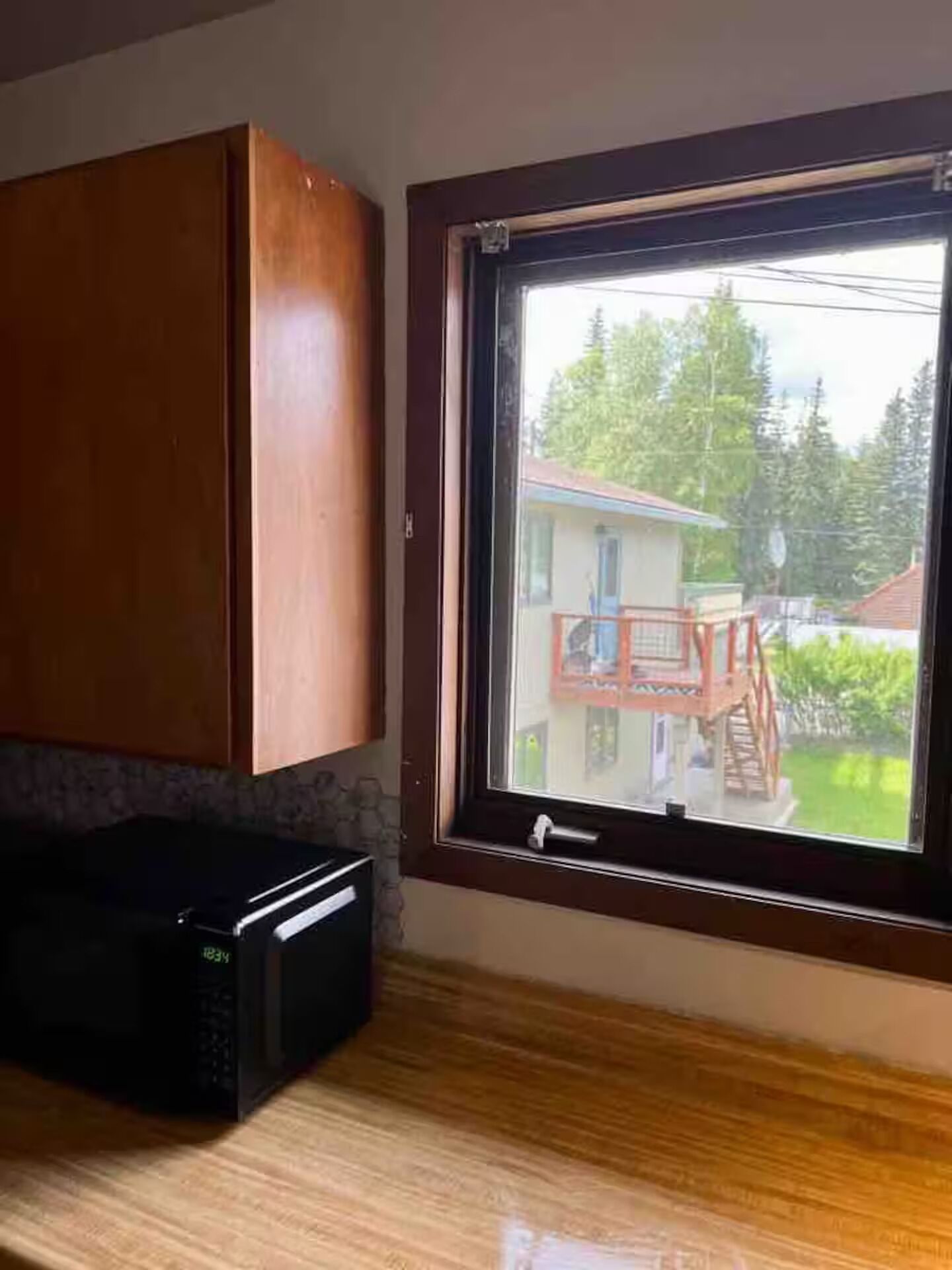 A kitchen with wooden cabinets, a microwave, and a window with a view of a house and trees.