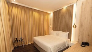 Une chambre d’hôtel avec un grand lit, un plancher en bois, une tête de lit en bois, une table de chevet et une chaise.