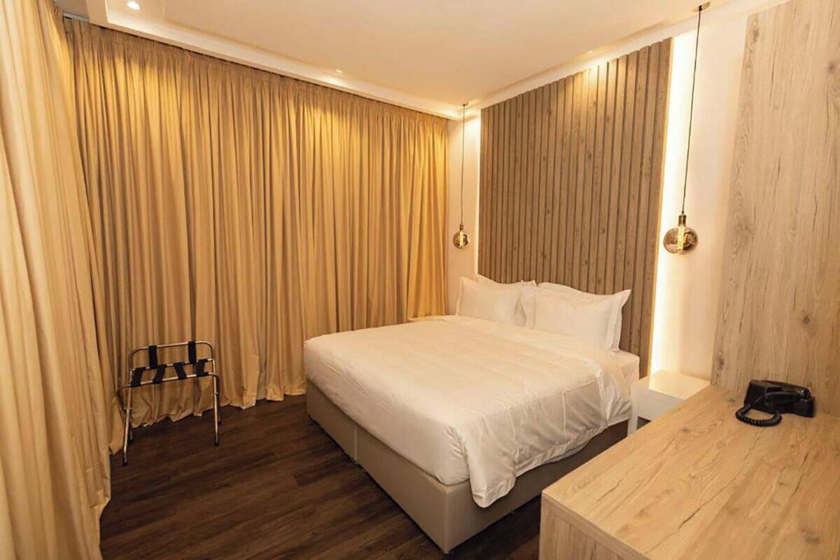 A hotel room with a large bed, wooden panel wall, and a bedside table with a lamp.
