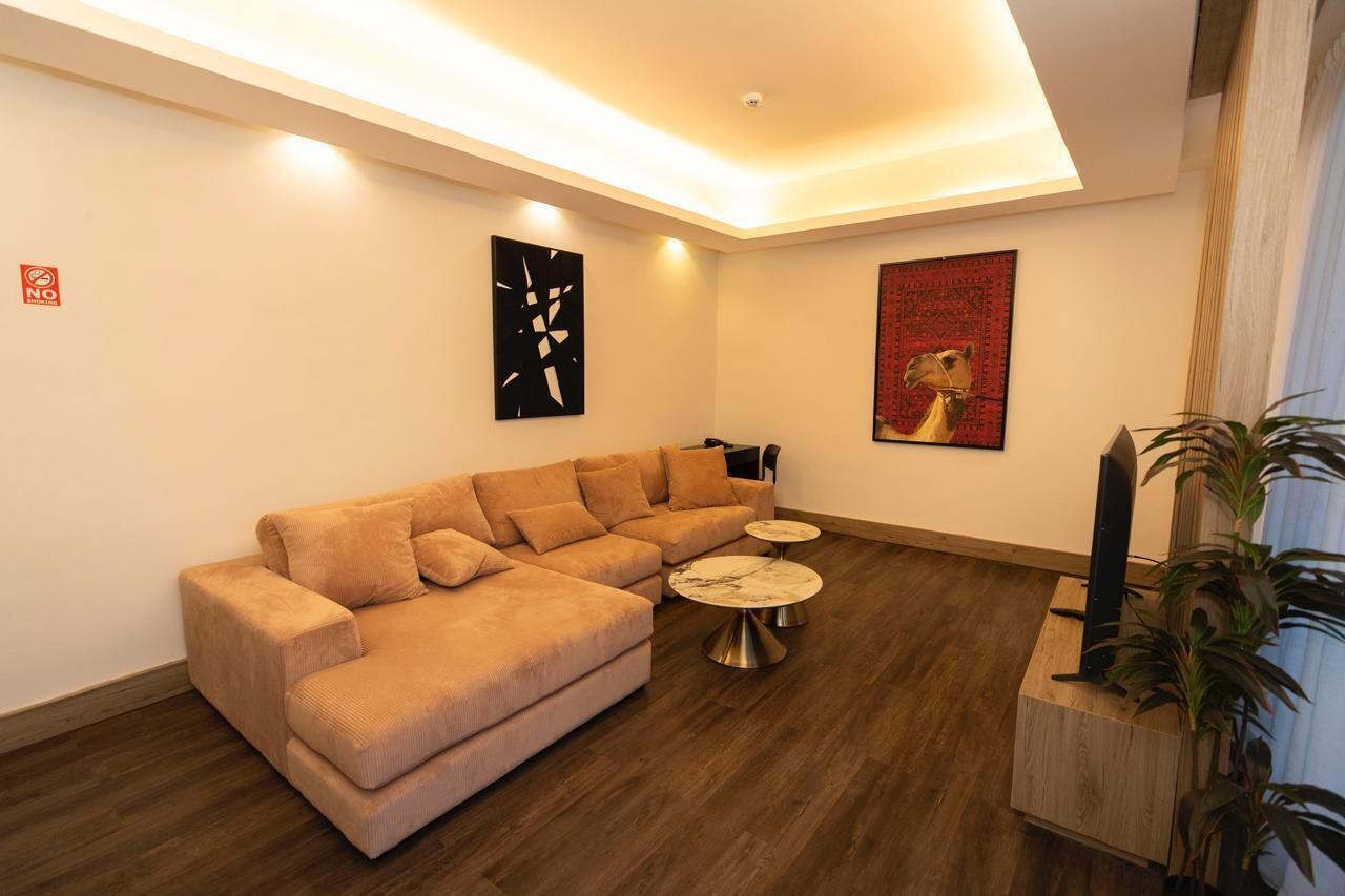 A modern living room with a beige sectional sofa, two small round coffee tables, and a large painting on the wall.
