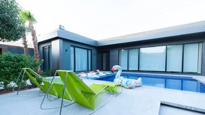 Un espace piscine extérieur moderne, avec une piscine à l’eau d’un bleu limpide, des chaises longues vertes et une petite piscine gonflable.
