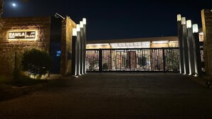 Une entrée fermée par un portail, donnant accès à un bâtiment doté d’une enseigne lumineuse et de luminaires verticaux.