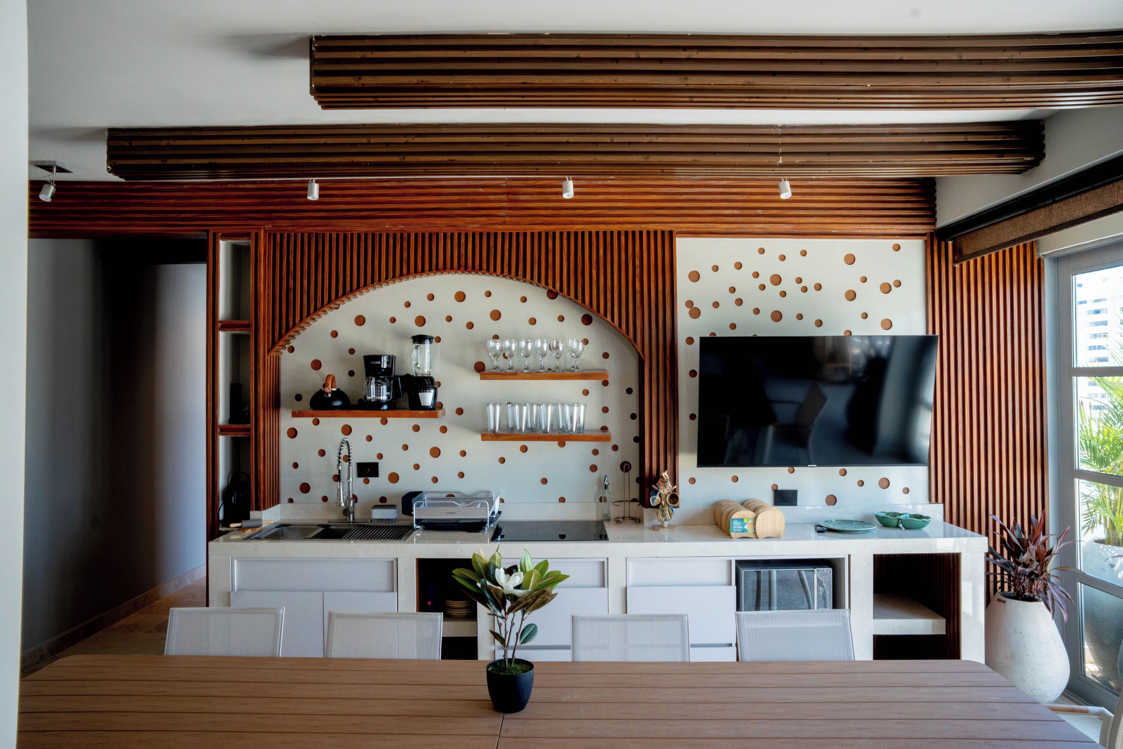 A modern kitchen with a built-in TV, wooden paneling, and a dining area with a table and chairs.