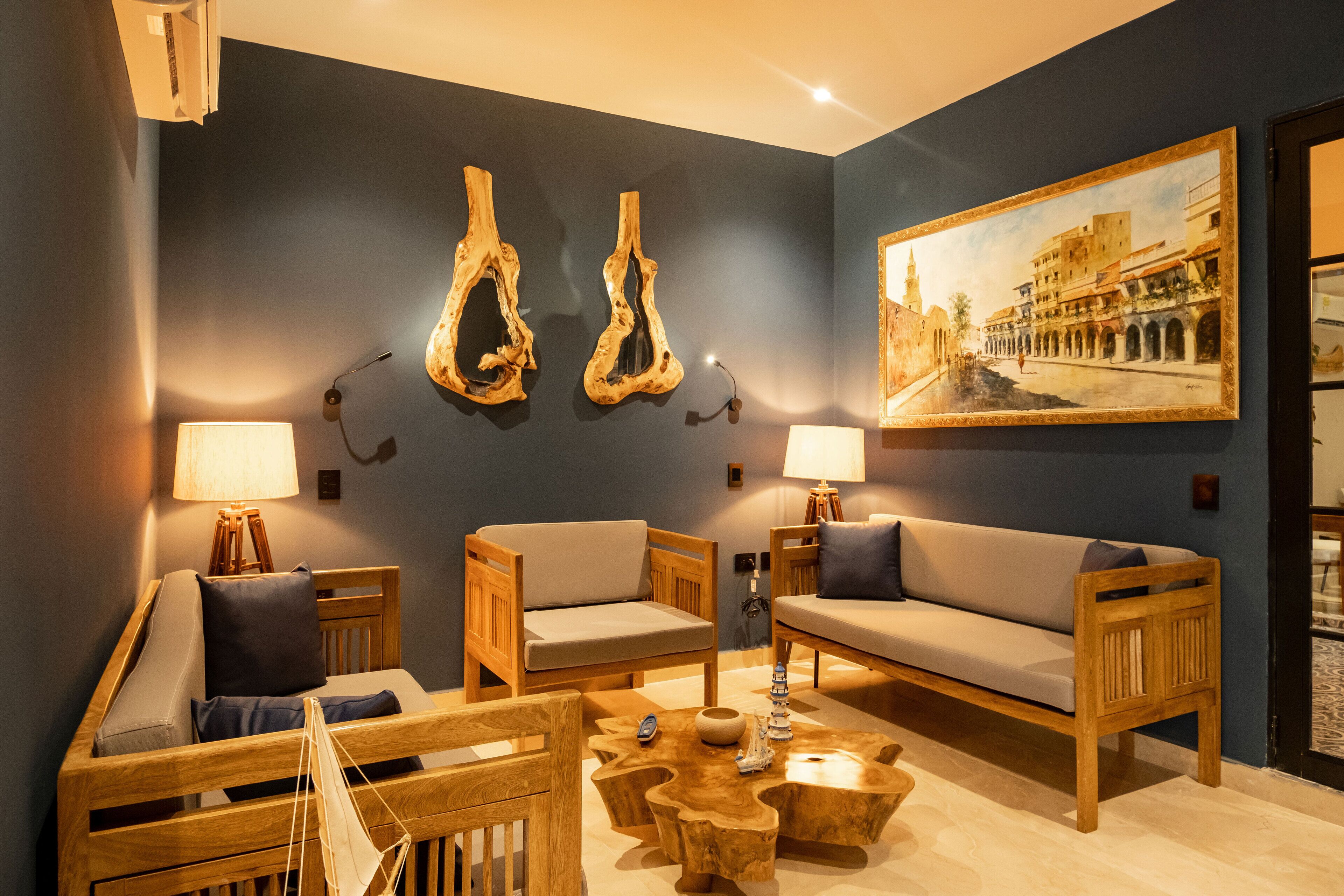 A cozy living room with wooden furniture, a painting of a street scene, and two wall-mounted wooden sculptures.
