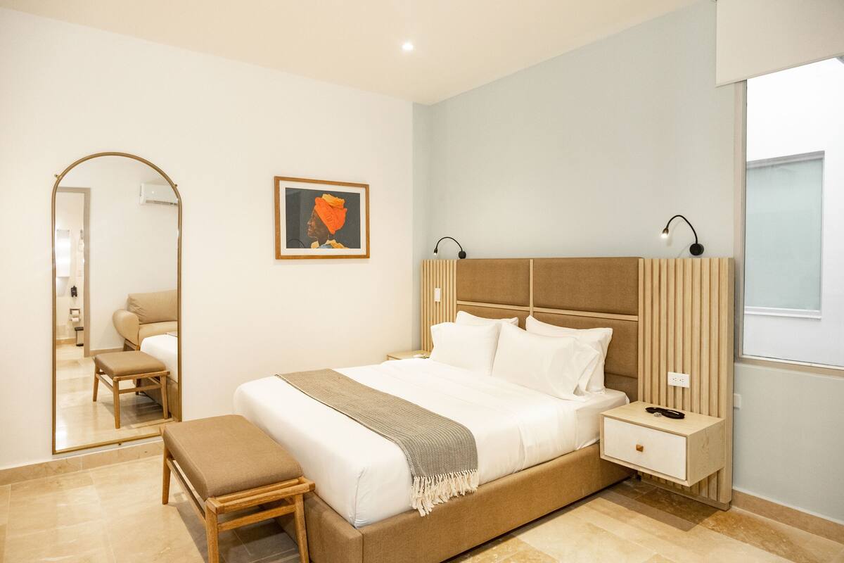 A modern bedroom with a large bed, bedside tables, a bench, a mirror, and a framed picture on the wall.