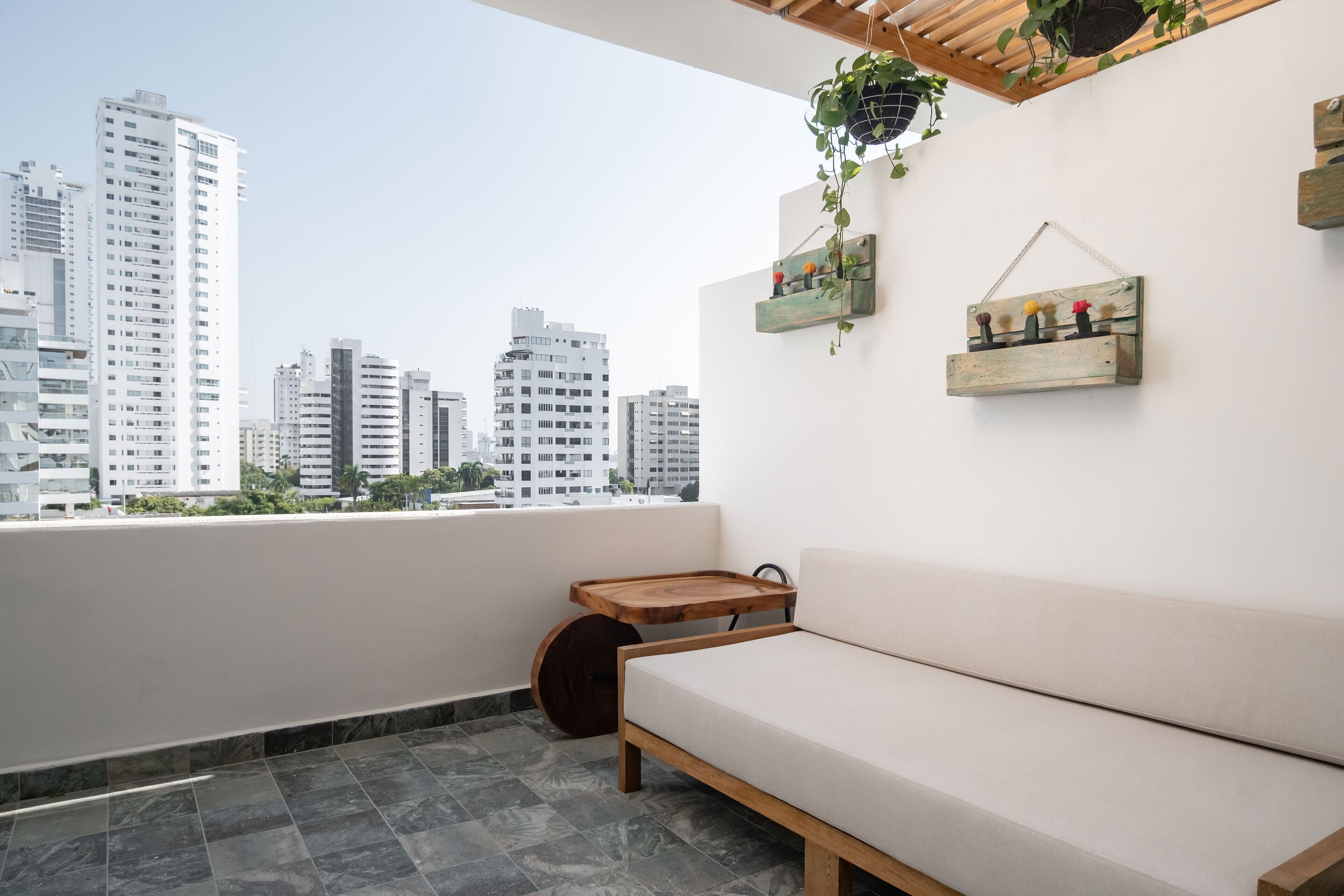 Un balcón con un sofá, una bandeja de madera y una planta colgante.