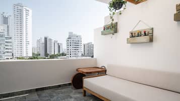 Un balcón con un sofá, una bandeja de madera y una planta colgante.