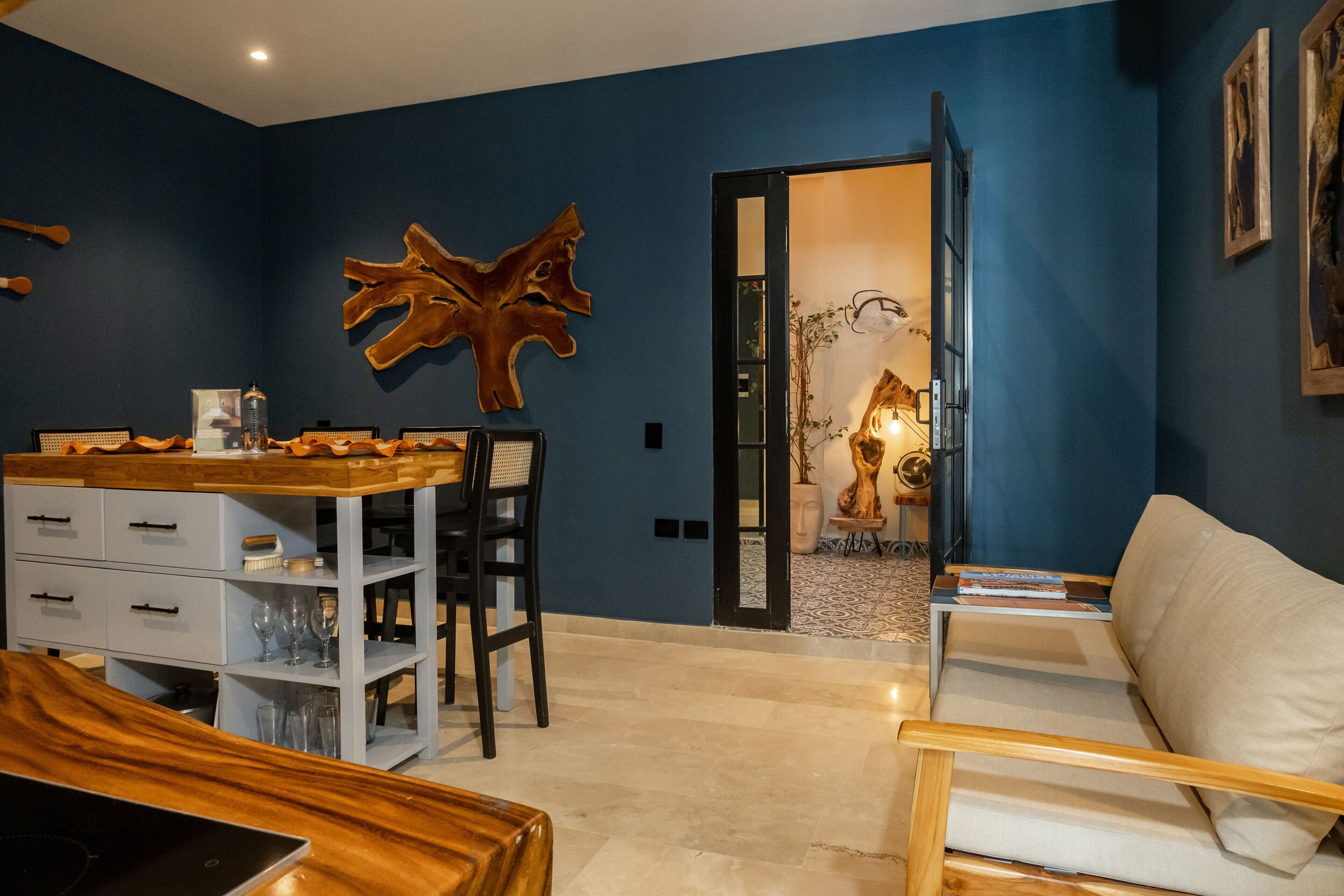 A modern living room with a blue accent wall, a wooden dining table, a sofa, and a decorative wooden sculpture.