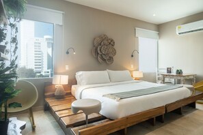Een moderne slaapkamer met een houten bed, twee bedlampjes, een decoratief object aan de muur en een uitzicht op gebouwen door een groot raam.