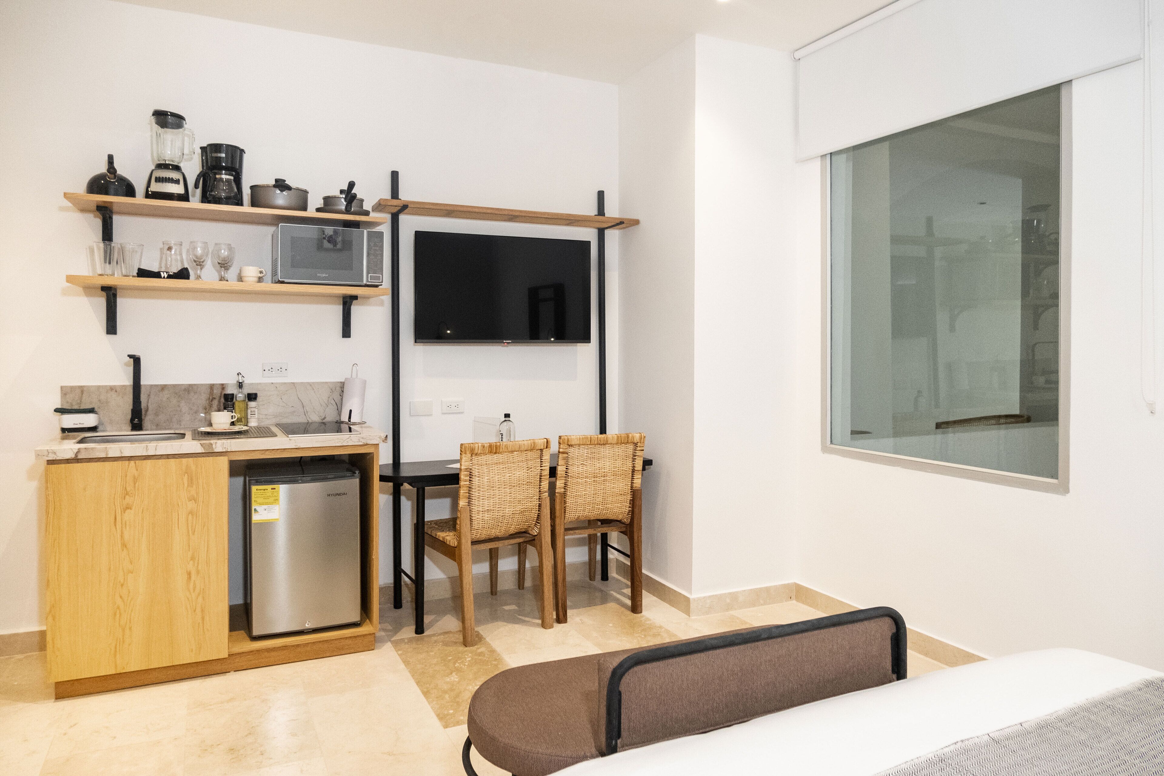 Eine kompakte Küche mit Kühlschrank, Mikrowelle und Kaffeemaschine, ein Essbereich mit Stühlen und ein großes Fenster mit Aussicht.