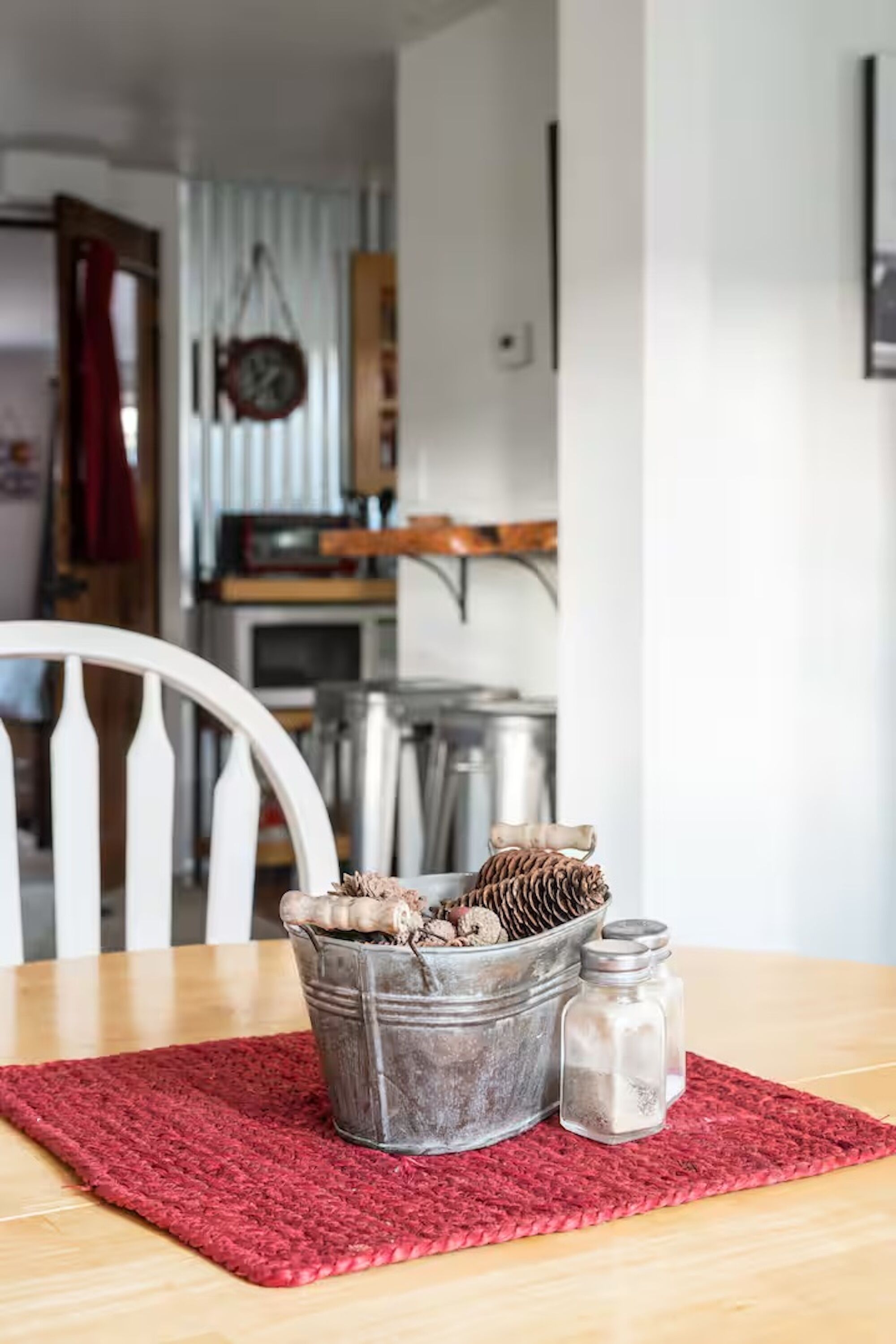 A dining table with a red rug, a metal bucket with pinecones, and salt shakers.