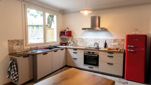 A kitchen with a window, a red microwave, a stainless steel range hood, a red refrigerator, and a wooden table. - 🏡 Large charming gîte in Fontevraud - Warm winter stays (6 to 12 pers) (Fontevraud-l'Abbaye)