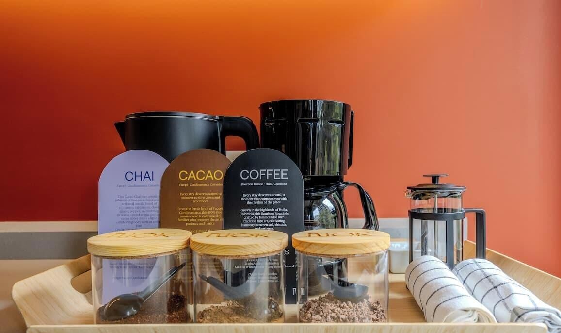 Una bandeja con equipo para preparar café y recipientes etiquetados de Chai, Cacao y Café.