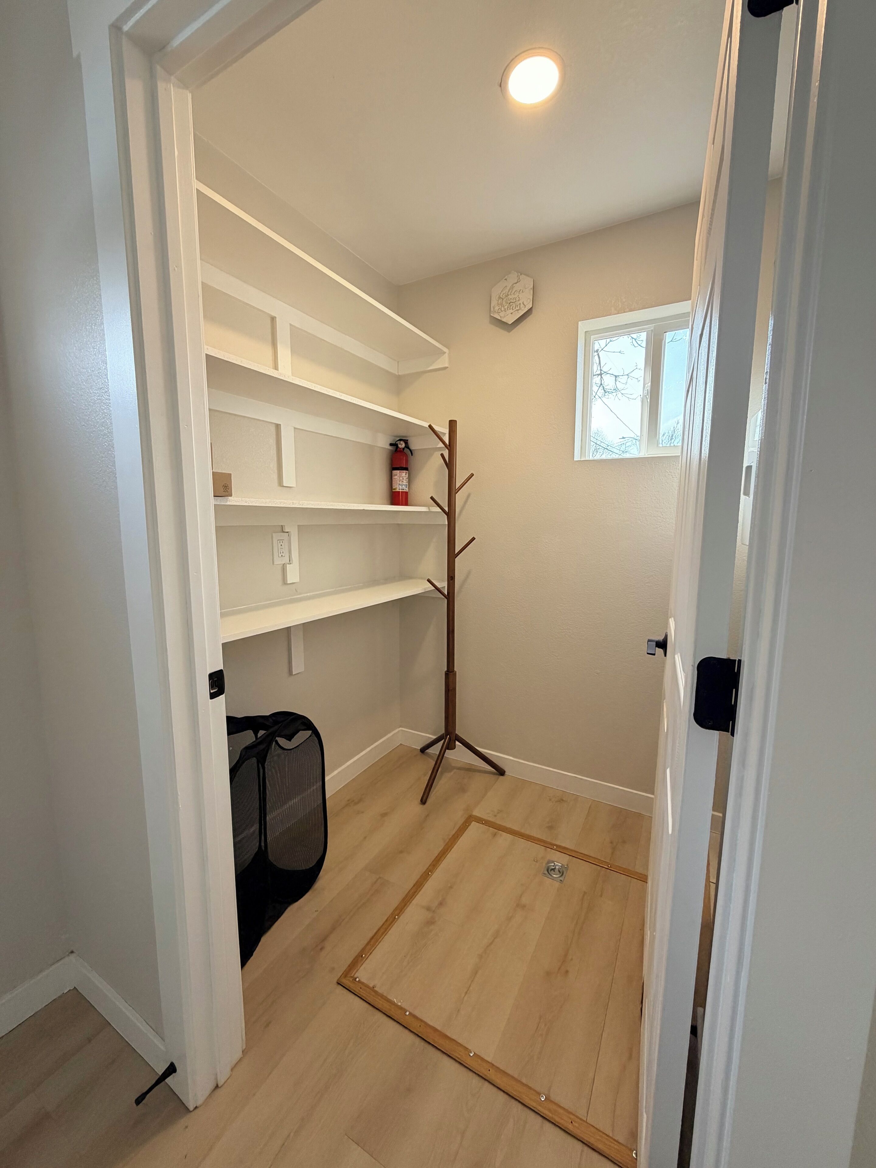 A room with a wooden floor, white walls, a window, a fire extinguisher, and a coat rack.