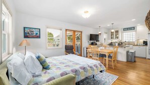 Un dormitorio acogedor con cama, mesita de noche y lámpara. Se ve un comedor con mesa y sillas. También se aprecia una cocina con fregadero y estufa.