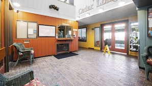 En entréhall med en receptionsdisk, flätade fåtöljer, en öppen spis och en skylt som välkomnar besökare till Cedar Lodge.