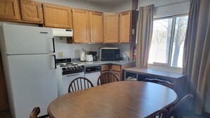 A kitchen with wooden cabinets, a white refrigerator, a stove, a microwave, and a dining table with chairs. - LAKEFRONT 2-bedroom Chateau Getaway at Whitecap Mountains Resort Unit 3 (Upson)