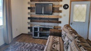 A living room with a mounted TV, wooden wall paneling, a door with blinds, and a patterned rug. - LAKEFRONT 2-bedroom Chateau Getaway at Whitecap Mountains Resort Unit 3 (Upson)