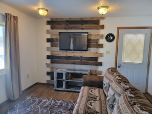 A living room with a mounted TV, wooden wall paneling, a door with blinds, and a patterned rug. - LAKEFRONT 2-bedroom Chateau Getaway at Whitecap Mountains Resort Unit 3 (Upson)