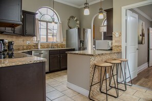 Cocina moderna con armarios oscuros, encimera de granito, refrigerador de acero inoxidable, horno empotrado y una ventana con cortinas.
