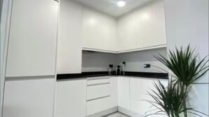 A modern kitchen with white cabinets, a black countertop, and a potted plant. - Madrid comfort suites (Aluche)