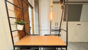 A dining area with a wooden table and black metal chairs, a hanging plant, and a unique light fixture. - Madrid comfort suites (Aluche)