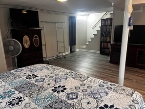 A bedroom with a patterned bedspread, a standing fan, a dresser, a TV, a bookshelf, and a staircase leading to another level. - Spacious 4-bedroom house in charming Bluff City (Bluff City)