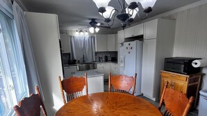 Ein Essbereich mit einem runden Holztisch und Stühlen, einem Deckenventilator und einer Küche im Hintergrund.