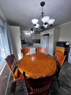 A dining area with a round wooden table and chairs, a ceiling fan, and a kitchen in the background. - Spacious 4-bedroom house in charming Bluff City (Bluff City)