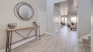 Un pasillo moderno con una consola de madera, un espejo redondo y una puerta que da a un comedor.
