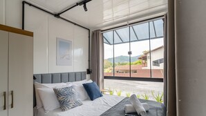 Una camera da letto con un letto, un quadro appeso, una finestra vista edifici e un asciugamano sul letto.
