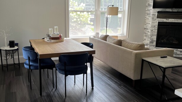 Una sala de estar moderna con chimenea, un comedor con mesa y sillas de madera, y un ventanal que proporciona luz natural.
