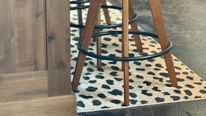 Una zona de bar con mostrador de madera, un taburete y un suelo con diseño.