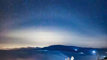 A night view of a mountainous landscape with a starry sky, a bridge, and a railing overlooking a valley.