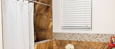 A bathroom with a shower curtain, a toilet, a bidet, a vanity with drawers, and a window with blinds.
