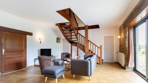 Amplia sala de estar con escalera de madera, un ventanal grande y una pared de piedra.