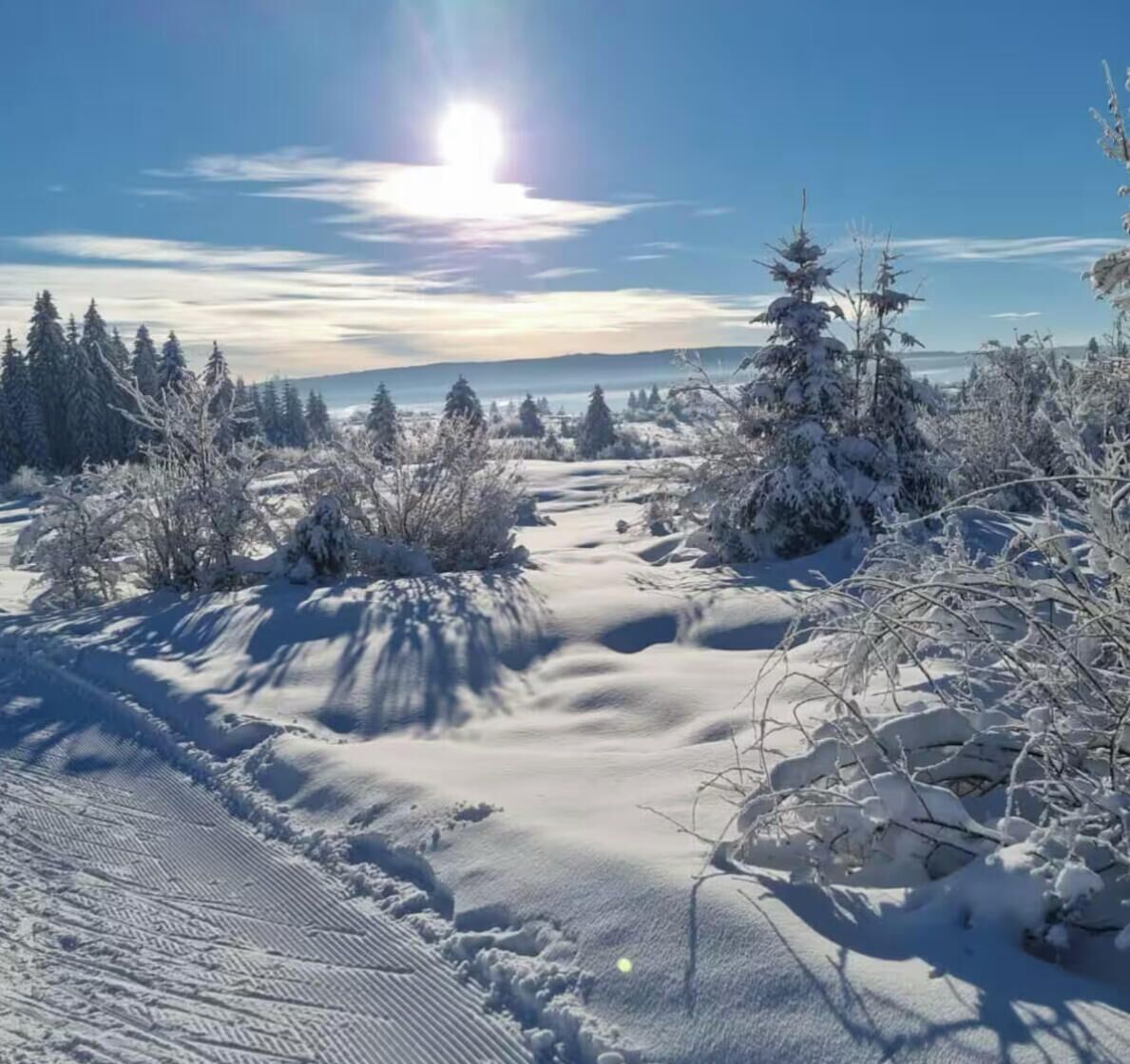 A snowy landscape with a clear sky and a visible sun.