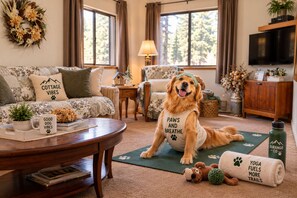 A cozy living room with a dog wearing a 'Paws and Breathe' vest, a coffee table with books, a fireplace, and a television. - Charming 1-bedroom cottage perfect for a relaxing Durango getaway (Durango)