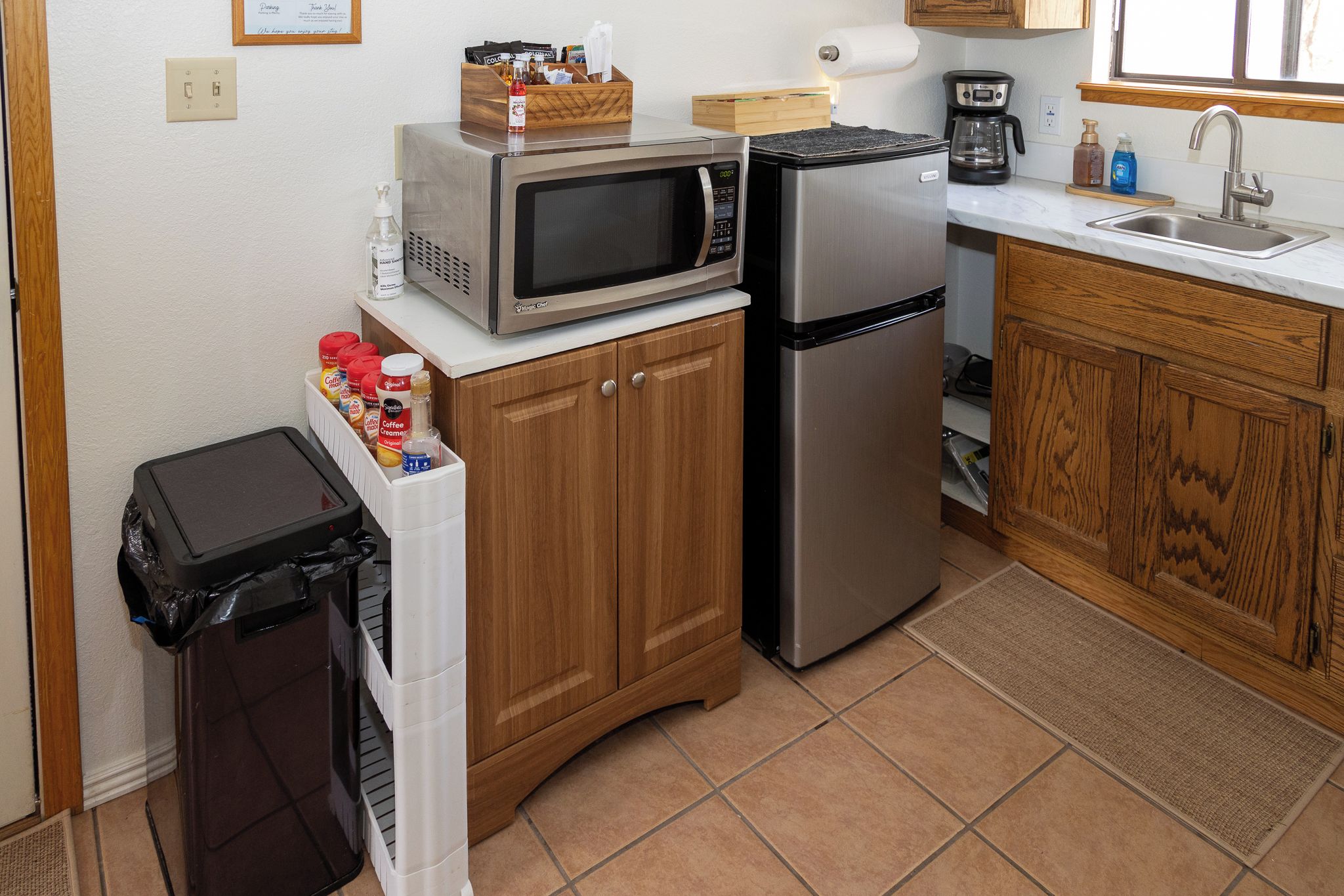 Une cuisine de taille réduite équipée d’un four à micro-ondes, d’un réfrigérateur et de meubles de rangement en bois.