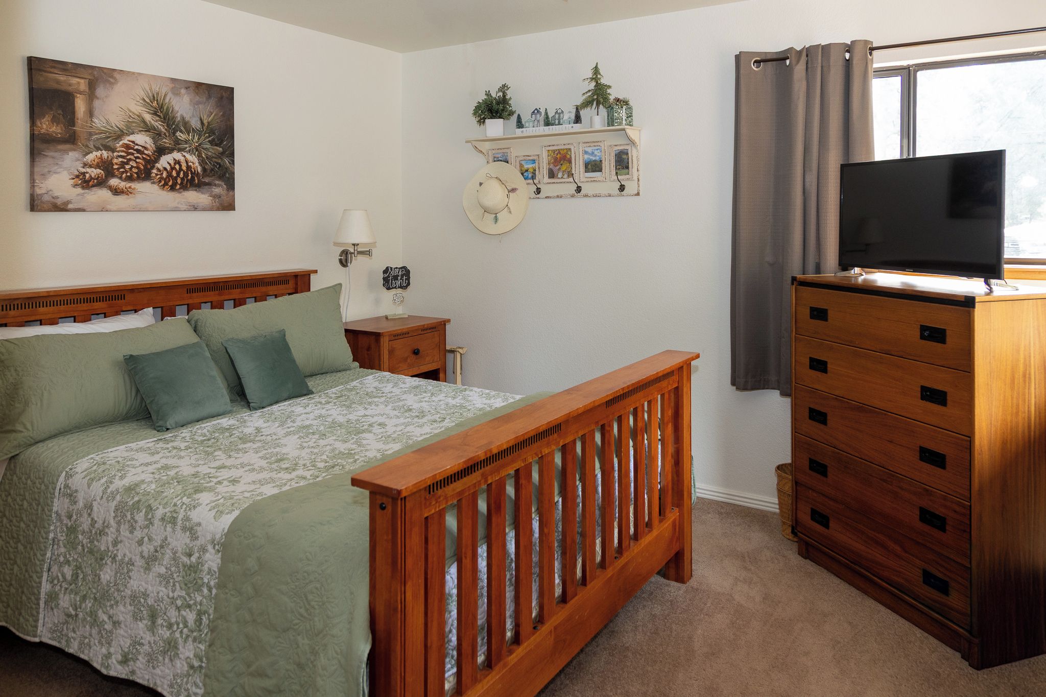 Une chambre à coucher avec un lit en bois, une commode, un téléviseur et une étagère murale agrémentée d’objets décoratifs.