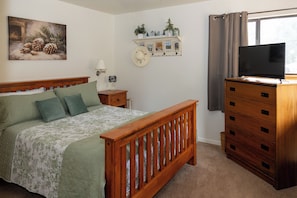 A bedroom with a wooden bed, a dresser, a television, and a wall-mounted shelf with decorative items. - Charming 1-bedroom cottage perfect for a relaxing Durango getaway (Durango)
