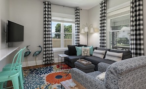 A living room with a sofa, a small table, a flat-screen TV, and a window with curtains.