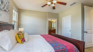 Une chambre à coucher avec un lit, un ventilateur de plafond, une fenêtre et une porte.
